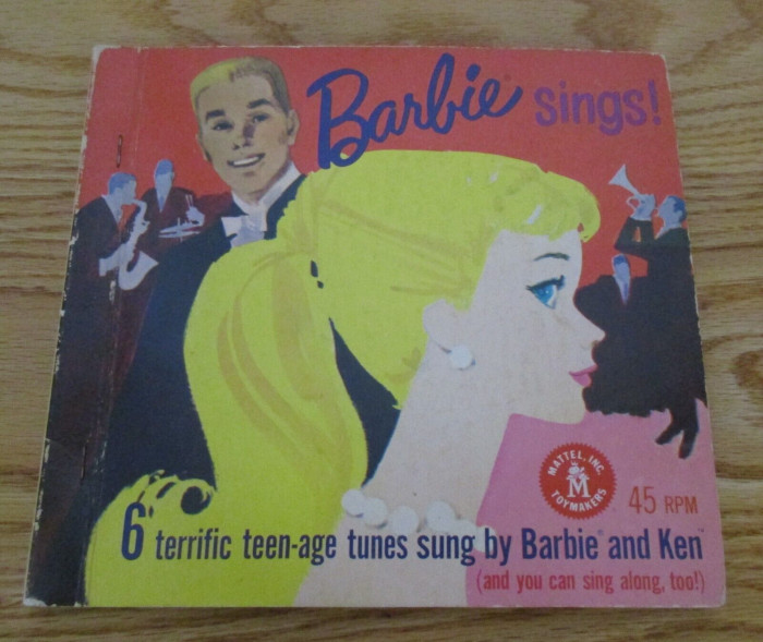 An album cover. Blonde ponytail Barbie is shown in closeup profile, wearing pearls. Ken and a band are behind her. The text reads:
Barbie (R) sings!
MATTEL, INC. TOYMAKERS
45 RPM
6 terrific teen-age tunes sung by Barbie (R) and Ken TM
(and you can sing along, too!)