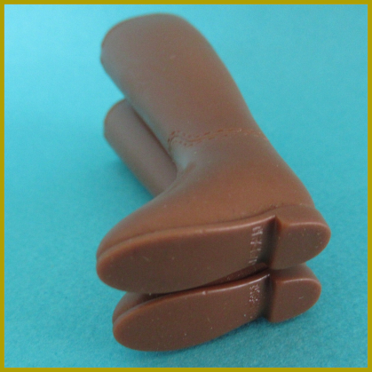 On a teal surface, a pair of high brown boots with low heels lie on their side, soled pointed toward the camera. The word JAPAN is printed on each sole.