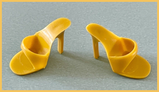 A pair of mustard-colored open-toed heels are displayed on a silvery grey background.