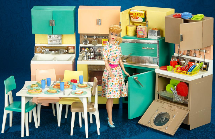 Photograph of the Deluxe Dream Kitchen, including a sink, oven/range, refrigerator, and dishwasher with front window, each with a cabinet overhead. A table and four chairs are also displayed. The table is white, each chair is a different pastel color (pink, teal, yellow and brown), and the cabinets and appliances are color-matched to the chairs. Dishes in red, blue, and green sit on the table, in the dishwasher and on a drying rack. Boxed food ingredients, a flour container, a toaster with toast poking out, and other food items are displayed, and cooking utensils hang from a rack above the dishwasher. A ponytail doll wearing Barbie Learns to Cook is posted in the scene.