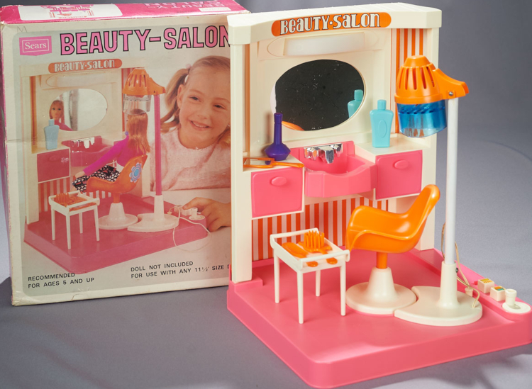 Sears Beauty Salon in mostly pink, orange and white, includes a revolving chair with working dryer, a small table for holding bushes and rollers, counter with non-functioning sink, and two working drawers beneath the counter.