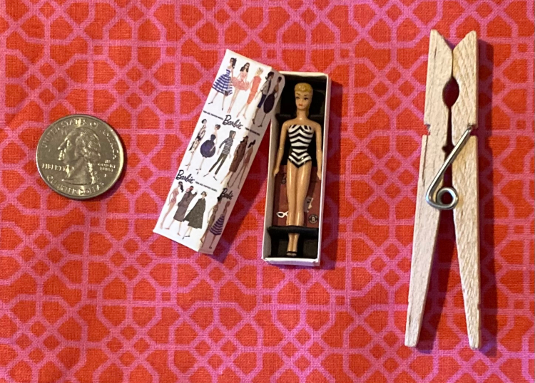 Boxed mini Barbie wearing zebra swimsuit. A circa-1960 booklet repro, in miniature, peeks out behind her in the box. The box lid looks just like the box above, perhaps in a richer shade. To either side lie a quarter and a clothespin for scale--the box is longer but thinner than the quarter, shorter than the clothespin but about as wide--about 2" long.