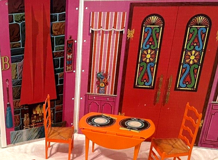 Vinyl house illustration. On one wall, rainbow-colored brick fireplace with red or orange hood, owl fireplace accessory, and warm fire. On the other wall, front double doors with bright stained glass, as well as windows shaded with red and pink vertically striped pattern. Between these, the walls are hot pink, Other wall hangings are a metal-look letter "B" and four butterflies in a frame. In the foreground are a drop-leaf table and two chairs in plastic, with place settings and wicker seats represented by stickers. (In product photos, this room has living room furniture). 