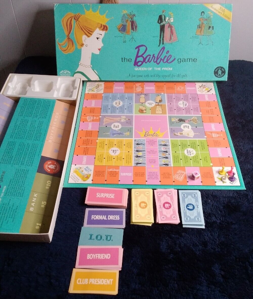 The reproduction game box looks like the original with a gold banner across the top right corner indicating it as a reproduction. The board has dominant pink and orange colors along with gold, green, blue and purple. Also shown are game money in yellow, pink and blue and cards: "Surprise," "Formal Dress," "I.O.U.," "Boyfriend," "Club President" in pink, purple, teal and gold, and the box lower lid with instructions and (unillustrated) sections for holding various cards.