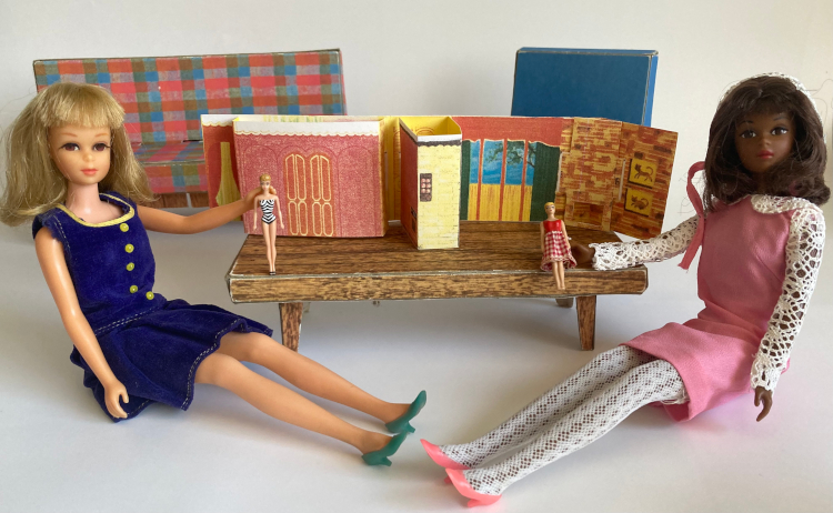 The mini new dream house sits on the Dream House coffee table, with sofa and chair still in background. The mini house is flipped around to show its interior, which resembles the full-sized house's with some simplifications. Most of the house is a single long piece of chipboard, but dimensional sections are inserted to represent Barbie's wardrobe and the kitchen counter with pass-through window (pass-through is not operational). In the foreground, two Francies sit on the floor, one holding a mini original ponytail Barbie in her chevron/zebra/debut swimsuit, and one holding a mini swirl ponytail Barbie in her original red swimsuit with a red-and-white cloth gingham kneelength skirt. The Francie at left wears a velvet-textured navy dress with pleated skirt and yellow buttons and trim (Pleat Neat). Francie at right wears a pink dress with white crocheted collar and cuffs, white lace tights, and pink heels (Dance Party, but with Iced Blue stockings). She also wears the white lace hood with pink trim but it's mostly hidden behind her head.