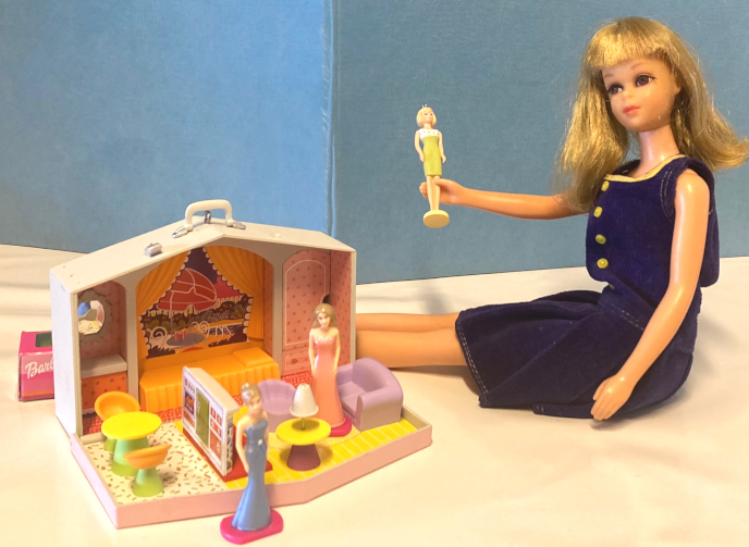 Francie in Pleat Neat is seated next to the Hallmark case house. In her hand is the mini Hallmark Barbie in Lunch on the Terrace. In and in front of the house are two mini Barbies in generic bare-shouldered evening gowns, one pink and one blue. THeir hair is ashy blonde, similar to Francie's. One wears hers long, down her shoulders, and one in a bun updo. The end of a hot pink box with pink and orange stripes and the Barbie logo is just visible behind the house.