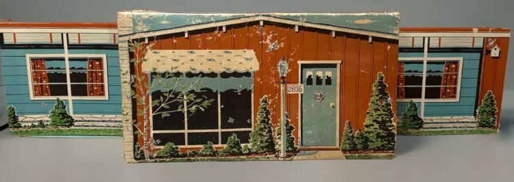 Color photo of a chipboard playset "house" in brown and blue. House exterior is lines with shrubbery, and a house number (2635) extends from a lamp post next to the windowpaned front door.