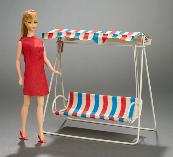 Blonde, blue-eyed T'n'T Barbie stands in a simple red shift dress and closed-toed heels. Next to her is a swing with awning that comes up a little above her shoulder. The frame is white metal and the seat and awning are striped red and blue on white. It looks wide enough to seat two, although it also looks low for Barbie, with the edge of the seat hitting at about her upper-mid calf.. 