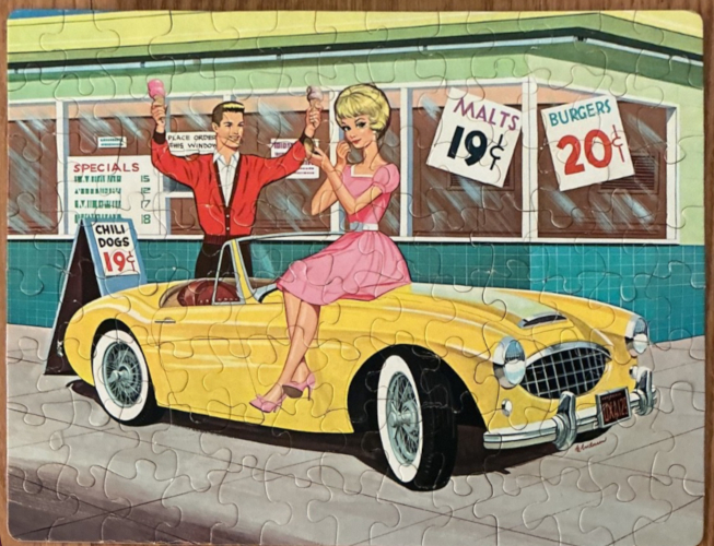 100-piece jigsaw puzzle, completed, bearing an illustration of blonde bubble cut Barbie in a pink dress sitting on a sporty yellow convertible. She is touching up her makeup. Behind her, Ken stands in a red sweater holding aloft two ice cream cones. The space behind him is filled with a hamburger stand with signs in the window like "Malts 19 c," "Burgers 20c." Chili dogs are also 19 cents. Barbie head looks too big for her body and is drawn with thicker lines.