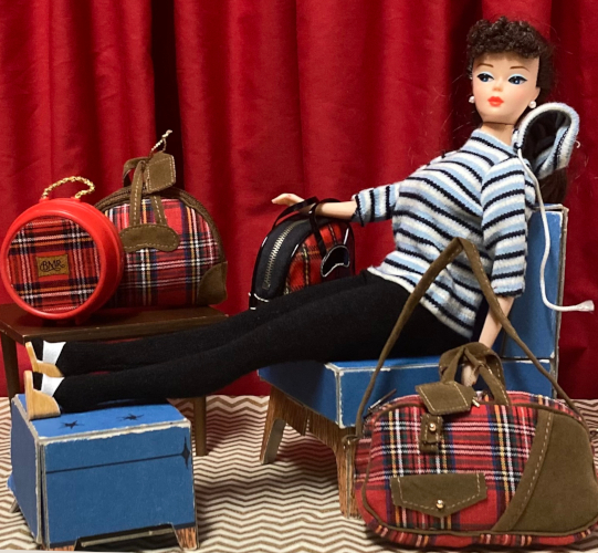 Brunette ponytail Barbie reproduction wears Winter Holiday: striped hoodie with half-length sleeves, black footed leggings, and platform shoes with white uppers. She sits in the blue chair with her feet on the matching ottoman (how else? this doll's legs don't bend). In one hand she holds her Winter Holiday overnight bag, about the size of a bowling bag in red plaid with black accents. At her side is a large soft-sided red plaid bag, not quite the same plaid, with brown leather-look straps and pouches and gold-toned buttons and whatnot. The brown leather, if I'm perfectly frank, is not that appealing. The bag has both short handles and long shoulder strap. The small brown table is toward the back and holds a smaller red plaid bag with brown leather, this one about the size and design of the one Barbie holds, plus a red hat box with rope handle and plaid printed on the front. Where is Kiki? She skipped this scene.