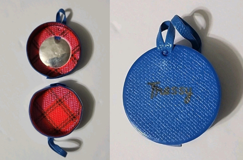 Two shots of Tressy's hat box taken from an eBay listing. At left, the box lies open in two pieces. The interior is lined with red-and-black plaid and one side holds a small circular bit of mirror. In the second image the hat box is closed. On the outside, it is blue with two blue straps, and the word Tressy in black script on the front.