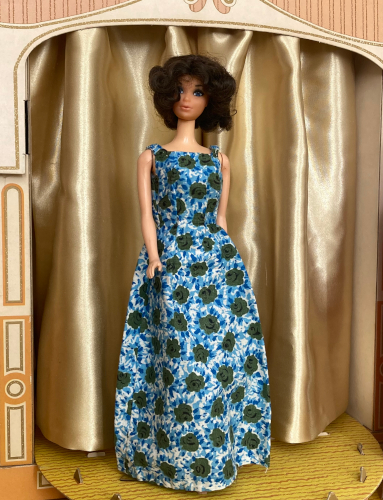 Over in the Fashion Shop, the Miss America Kelley doll with mussed hair stands wearing a floorlength, sleeveless dress with somewhat full skirt, with an allover pattern of blue and green flowers.