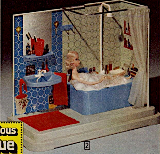 As described, two steps up to a plantform to which two walls are attached. On the londer of the two walls are a tub and washstand, backed by blue and white tile. Over the sink on a narrow ledge sits a cup with toothbrushes. A red towel hangs next to the sink and a red floormat sits beneath. Next to this is blue bathtub with a shower head extending up and a shower curtain drawn back. BLonde Quick Curl Barbie sits in the tub, covered in bubbles (this is one of the images from the top of the post).