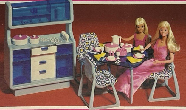 Product image from Dream Furniture packagibg. Blonde Superstar Barbie and matching Skipper sit at a plastic dining table with clear blue surface. The table is laden with pink-and-white dishes and cookware and yellow cloth napkins. The Eames-style chairs have a funky geometric print in blue, white, and yellow covering the molded seats. Nearby sits a dining room hutch in light blue molded plastic with white draws are translucent blue doors.