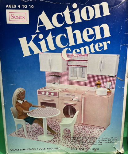 Packaging for Action Kitchen Center as described in the text. The kitchen wall component is smaller, with the dishwasher beneath the sink and a half-sized fridge adjacent; all the appliances and counters are the same sandy pink, while the splash guard and table surface are bolder pink-and-white checks. The chairs are white molded plastic with four legs and armrests like you find outdoors. There is totally unacceptable pink-and-white tiger-striped flooring. Malibu Barbie sits at the table. Text says "Ages 4 to 10, Sears, Action Kitchen Center, Unassembled - No tools required," plus some mostly undiscernable small text including "play vegetables."