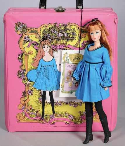 Red-haired TNT Barbie stands in front of a pink mod Barbie carrying case. On the carrying case, a character is depicted wearing a black-trimmed, blue babydoll dress with wide bell sleeves and black tights. The doll in the picture is wearing the same dress with black tights and boots. The dress has a homemade appearance.